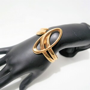 May include: Gold-toned metal bracelet with an abstract design featuring overlapping circles and curves.