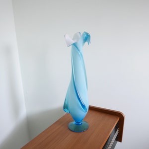May include: A blue and white glass vase with a swirling design. The vase is tall and slender, with a wide mouth and a narrow base.