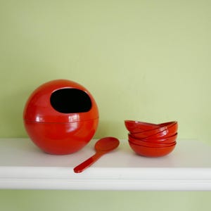 Peut inclure: Un ensemble de bols rouges emboîtables avec une cuillère rouge assortie et un bol rouge en forme de sphère avec un trou sur le dessus.