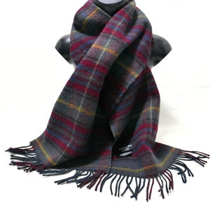 May include: A gray, red, blue, and yellow plaid scarf with fringe. The scarf has a label that reads "Christian Dior" in black text.