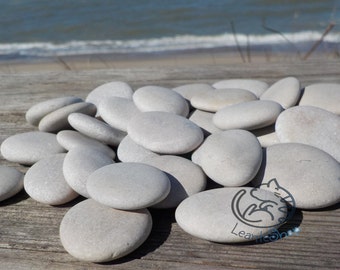 May include: A pile of smooth, white river stones on a wooden surface. The stones are various sizes and shapes, and they are all a light grey colour.
