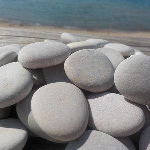 May include: A pile of smooth, light gray stones, some with a slightly rough texture, arranged in a random pattern. The stones are all different sizes and shapes, and they are all very close together.
