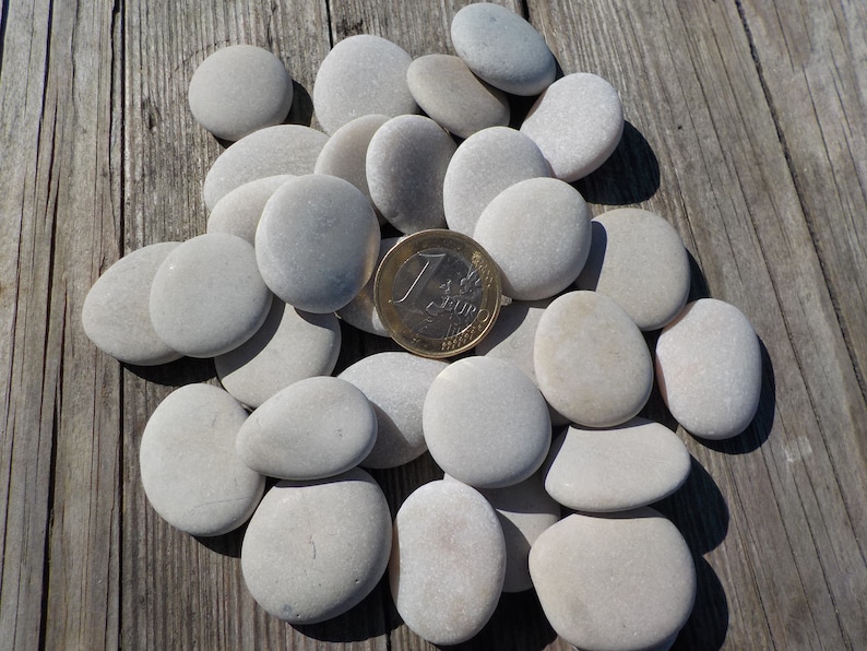 May include: A collection of smooth, white, round stones of various sizes. A single euro coin is placed in the center of the pile of stones.