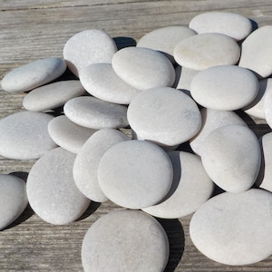 May include: A collection of smooth, white river rocks of various sizes. The rocks are arranged in a pile on a wooden surface.