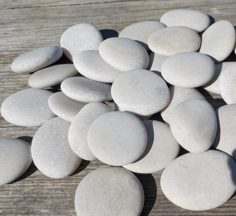May include: A collection of smooth, white river rocks of various sizes. The rocks are arranged in a pile on a wooden surface.