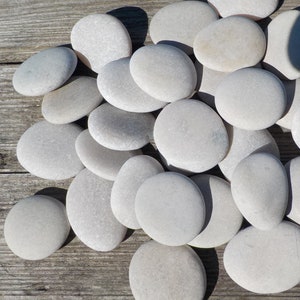 May include: A collection of smooth, white, oval-shaped stones arranged on a wooden surface. The stones are various sizes and have a natural, polished look.