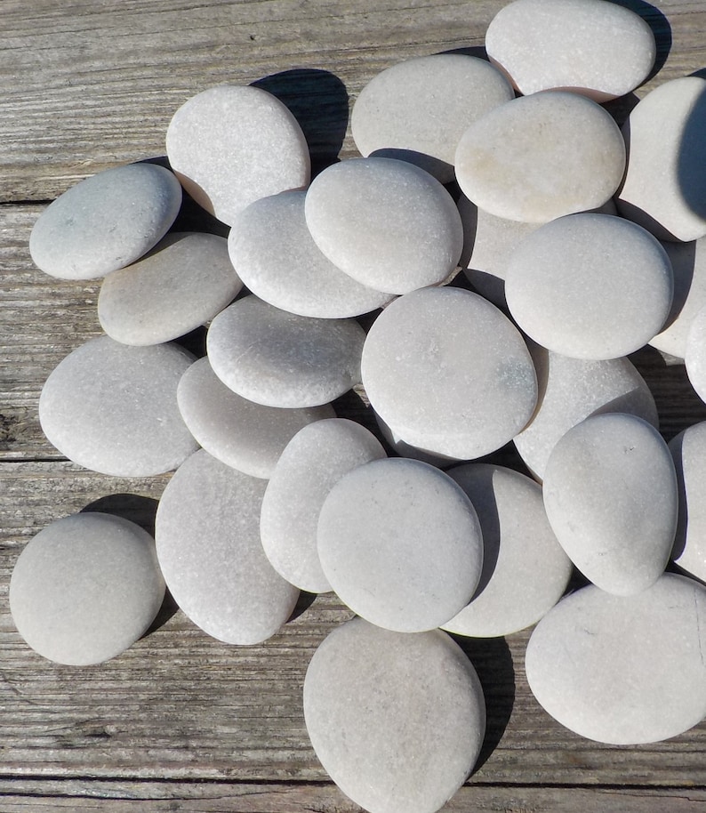 May include: A collection of smooth, white, oval-shaped stones arranged on a wooden surface. The stones are various sizes and have a natural, polished look.