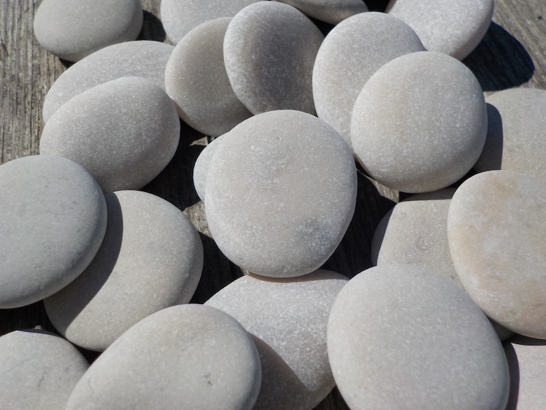 May include: A collection of smooth, light gray stones, some with a slightly rough texture, arranged in a random pattern on a wooden surface.