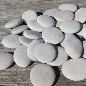 May include: A pile of smooth, light gray stones on a weathered wooden surface. The stones are various sizes and shapes, with a natural, polished finish.