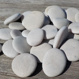 May include: A pile of smooth, white river rocks. The rocks are various sizes and shapes, and they are all very light in color.