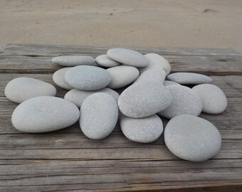May include: A pile of smooth, light gray stones on a weathered wooden surface. The stones are various sizes and shapes, with some stacked on top of others.