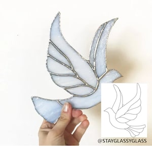 Peut inclure: Une colombe en vitrail avec un motif blanc et bleu. La colombe est en vol et a des ailes détaillées. Un dessin au trait de la colombe est présenté dans le coin inférieur droit de l'image. Le texte "@stayglassyglass" est sous le dessin.