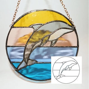 May include: A stained glass suncatcher depicting a dolphin leaping from the water. The suncatcher is circular and features a blue, white, orange and yellow colour scheme. The dolphin is grey and has a black outline.