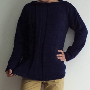 May include: A dark blue knitted sweater with long sleeves and a round neckline.