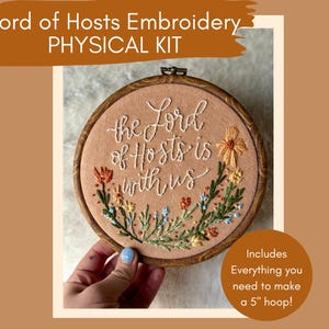 Puede incluir: Kit de bordado físico con un bastidor de madera. El kit incluye un bastidor de 12,7 cm y presenta el texto "the Lord of Hosts is with us" bordado con hilo blanco. Bordado floral en naranja, amarillo y azul.