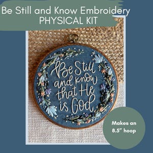 May include: A blue embroidery hoop with the text "Be Still and Know that He is God" in white script. The embroidery is decorated with floral and leaf accents. The kit makes a 21.6 cm hoop.