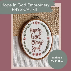 Puede incluir: Un bastidor de bordado ovalado con el texto "Hope in God O my Soul" en hilo marrón. El bordado está rodeado por un aro de madera marrón y un diseño de hojas verdes y marrones. El kit hace un aro de 12,7 cm x 17,8 cm.