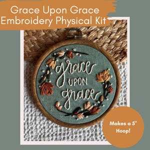 May include: A round embroidery hoop with the words "Grace Upon Grace" stitched in white thread on a teal fabric. The design includes autumn-colored leaves and a wooden hoop. The kit makes a 5-inch hoop.