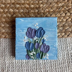 May include: Square canvas art featuring a bouquet of purple and blue tulips with green stems and white accents against a light blue background. The painting has a textured, impasto style.