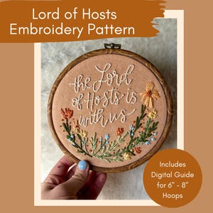 May include: A round embroidery hoop with the text "the Lord of Hosts is with us" in white thread. The design includes embroidered flowers in orange, yellow, and blue. The wooden hoop is designed for 6" - 8" hoops.