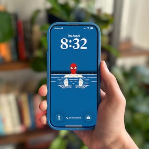Può includere: Uno smartphone con custodia blu mostra una schermata di blocco con sfondo blu e un'illustrazione grafica di un personaggio con maschera rossa che si rilassa in piscina. Lo schermo mostra l'ora 8:32, la data gio 6 ago e icone di stato.