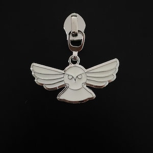 May include: A silver zipper pull featuring a white owl design. The owl has black eyes and is in flight.