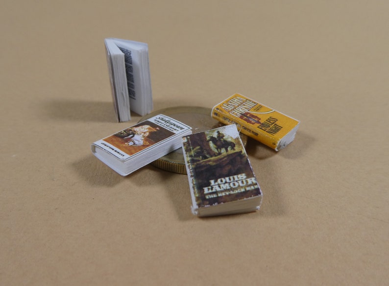 May include: Four miniature paperback books, including "Shadower" by Brenda Joyce, "The Renegade  Man" by Louis L'Amour, and "Santa  Fe" by  G.G.  Gregory. The books are on a brown surface with a gold coin.