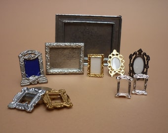 May include: A collection of miniature silver and gold picture frames. The frames are in various styles and sizes, including a large silver frame with a blue background.