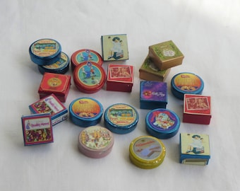 Op de afbeelding: Een verzameling vintage blikken doosjes met verschillende ontwerpen en kleuren. De doosjes bevatten afbeeldingen van kinderen, dieren en voedsel. Sommige doosjes hebben tekst, zoals "Quality Street" en "Milk Tray".