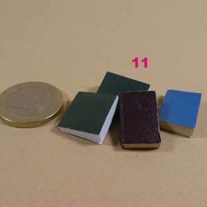 May include: Four miniature books, one green, one dark red, one blue, and one dark green, are arranged on a brown surface. The books are all about the same size and are smaller than a US one dollar coin.