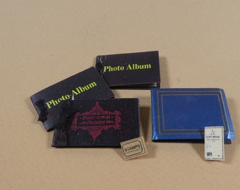 May include: A collection of vintage photo albums and ephemera. The albums are in various sizes and colors, including black and blue, with gold accents. Some albums have text that reads "Photo Album" and "Post Card Album". A small label reads "Stamps".
