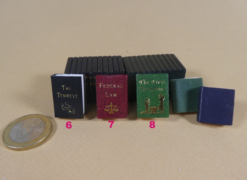 May include: A collection of miniature books with different colored covers. The books are titled "The Tempest", "Federal Law", "The First Christmas", and an unreadable title. The books are arranged in a row on a light brown surface.