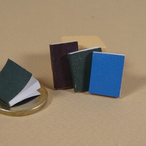 May include: Four small, bound books with textured covers. One book is dark purple, one is dark green, one is light green, and one is blue.