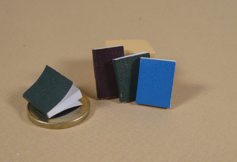 May include: Four small, bound books with textured covers. One book is dark purple, one is dark green, one is light green, and one is blue.