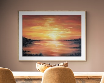 May include: A framed landscape painting depicts a sunset over water, with warm orange and yellow hues dominating the sky and reflecting on the water. The artwork is in a light wood frame, hanging above a wooden table with three mustard-colored chairs.