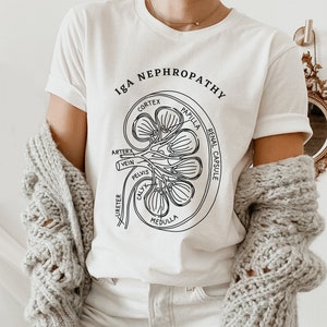 May include: White t-shirt with a black line drawing of a kidney and the text "IgA Nephropathy". The drawing includes labels for the different parts of the kidney, including the cortex, medulla, papilla, renal capsule, artery, vein, pelvis, and calyx.