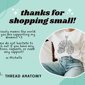 May include: A white t-shirt with a black line drawing of lungs with text inside each lung. The text reads "I breathe in love" and "I exhale kindness". The t-shirt is on a person wearing blue jeans and sitting on a wooden chair. The background is a light blue and green abstract design with the text "thanks for shopping small!" and "it seriously means the world that you are supporting my dreams! <3 please do not hesitate to reach out if you have any questions, requests, or need any support! xx Michelle THREAD ANATOMY".