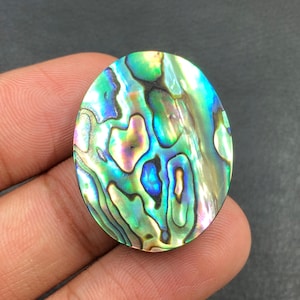 May include: Oval-shaped abalone shell cabochon with iridescent colors of green, blue, and purple. The polished surface displays a swirling pattern of natural colors. This gemstone is suitable for jewelry making or crafting.
