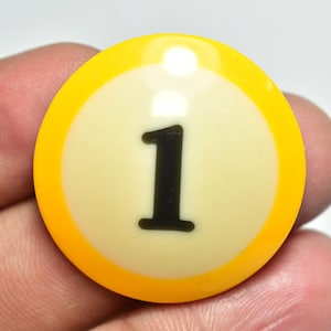 Puede incluir: Una bola de billar amarilla y crema con el número 1 en negro. La bola tiene un acabado brillante y está diseñada para su uso en un juego de billar. La bola es redonda y tiene un borde amarillo.