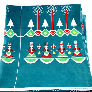 May include: Teal fabric with a repeating pattern of stylized figures, trees, and geometric shapes in red, white, and green. The design includes figures with heart-shaped accents and tree-like elements.