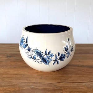 May include: A white ceramic planter with a blue floral design. The planter has a round shape and a wide opening.