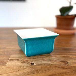 May include: A teal blue ceramic dish with a white interior. The dish is sitting on a wooden table.