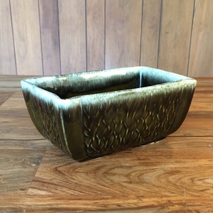 May include: A rectangular ceramic planter with a green glaze and a white interior. The planter has a textured surface with a woven pattern.