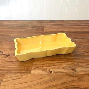 May include: A yellow ceramic serving dish with a wavy edge. The dish is on a wooden surface.