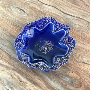 May include: A cobalt blue ceramic bowl with a scalloped edge and intricate gold floral designs. The bowl is nested inside a slightly larger bowl with the same design.