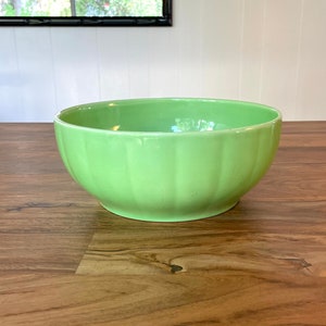 May include: A light green ceramic bowl with a fluted design. The bowl is sitting on a wooden surface.