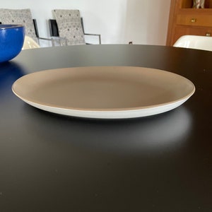 May include: A brown oval serving platter with a white rim sits on a black table.