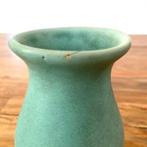 May include: A celadon green ceramic vase with a flared rim and a textured surface. The vase has a crackled appearance and a small chip on the rim. The vase is a decorative item.