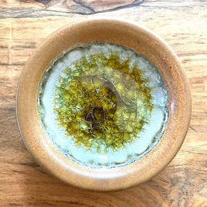 May include: A small, round ceramic bowl with a brown rim and a green and white crackle glaze.