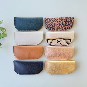 May include: Eight different colored leather eyeglass cases. The cases are all half-moon shaped and have a stitched edge. One case has a leopard print pattern.